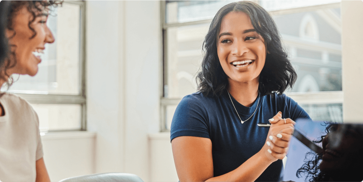 Duas mulheres felizes e sorridentes em uma sala de reuniões.